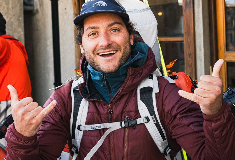 Hiking backpack, Burgundy jacket, Blue cap, Layered clothing, Outdoor gear